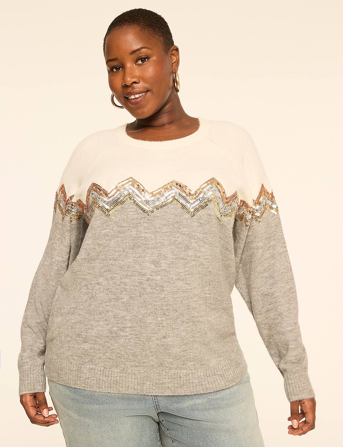 A woman in a light grey and cream sweater with a sequined zigzag pattern stands against a plain, light-colored background. Product Image 1