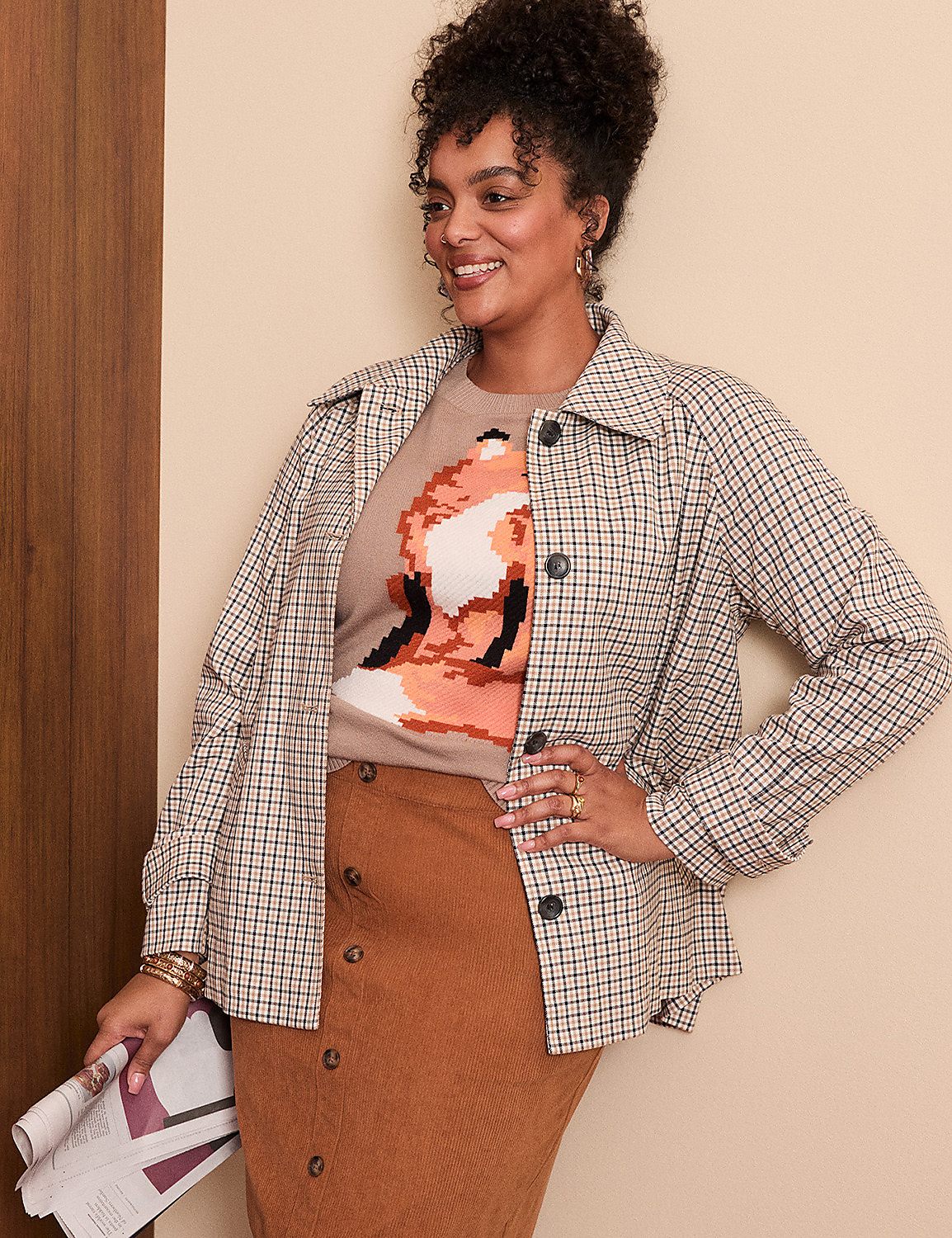 A woman in a plaid jacket and brown corduroy skirt poses in front of a neutral wall with a wooden accent. Product Image 4