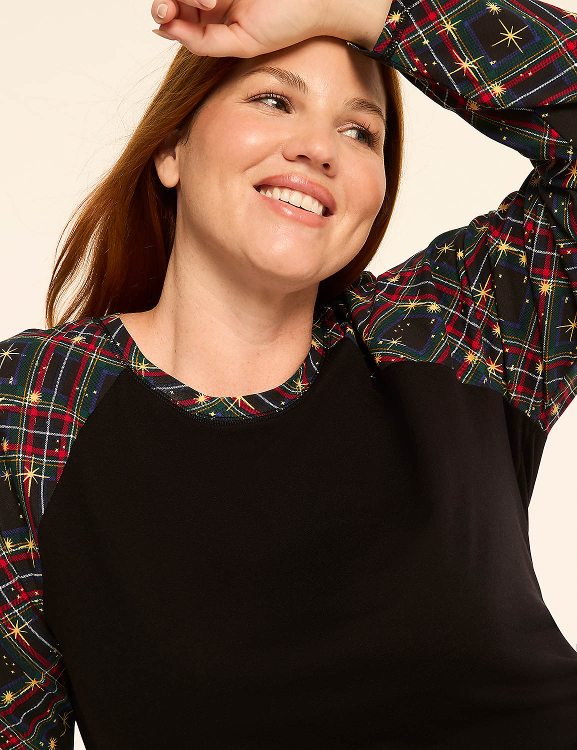 A smiling woman with auburn hair wears a black shirt with plaid sleeves, set against a plain, light-colored background. Product Image 3