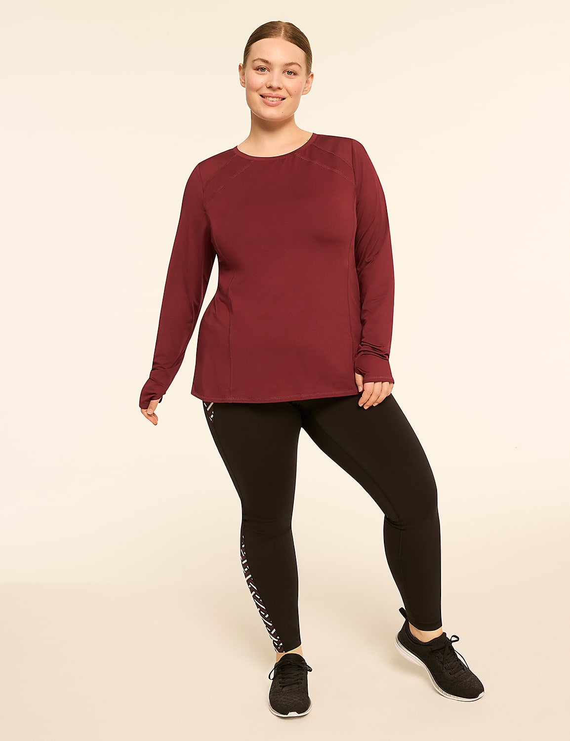A smiling woman in a maroon long-sleeved shirt and black leggings stands against a plain, light-colored background. Product Image 3