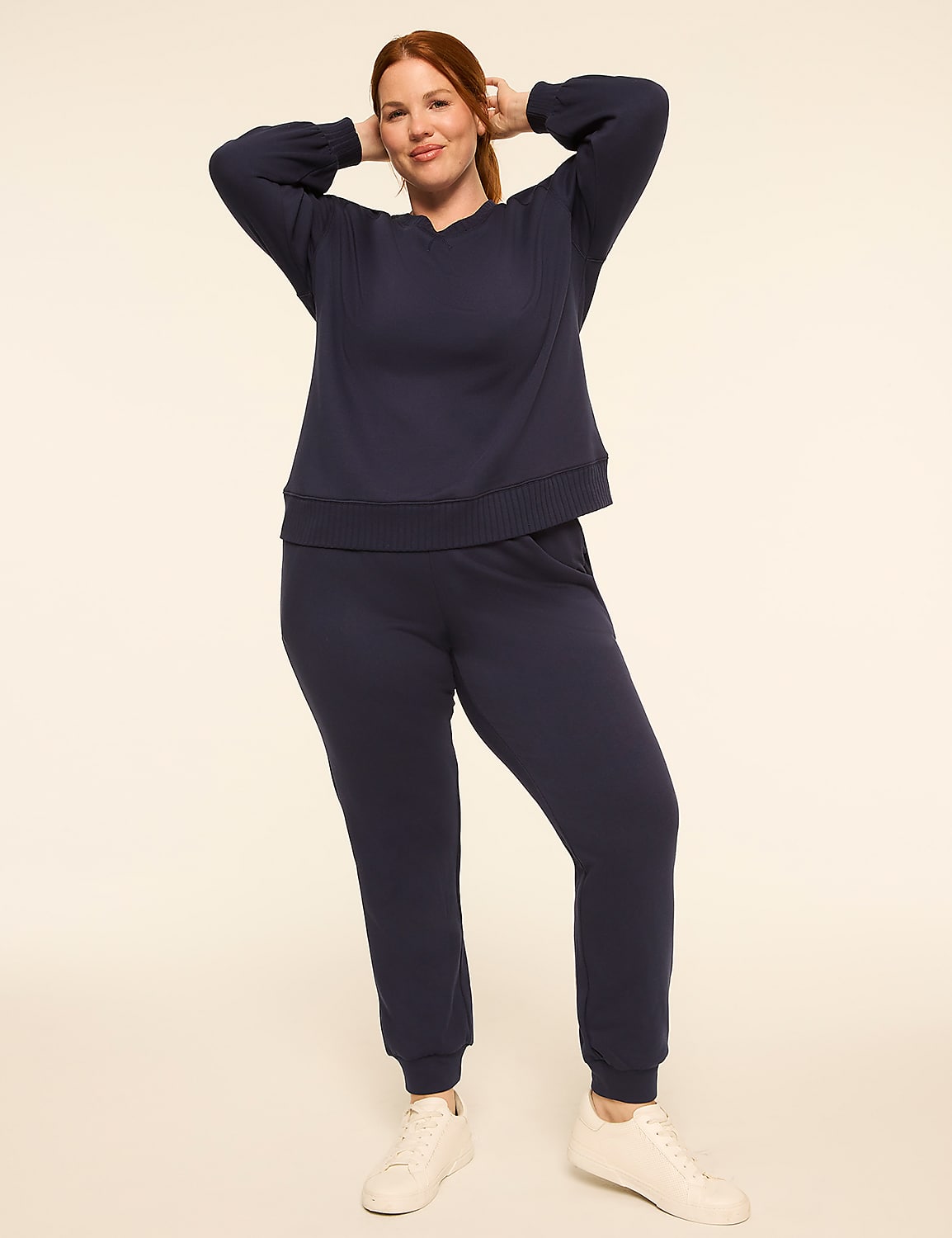A woman in a navy blue loungewear set poses with her hands behind her head against a plain, light-colored background. Product Image 3