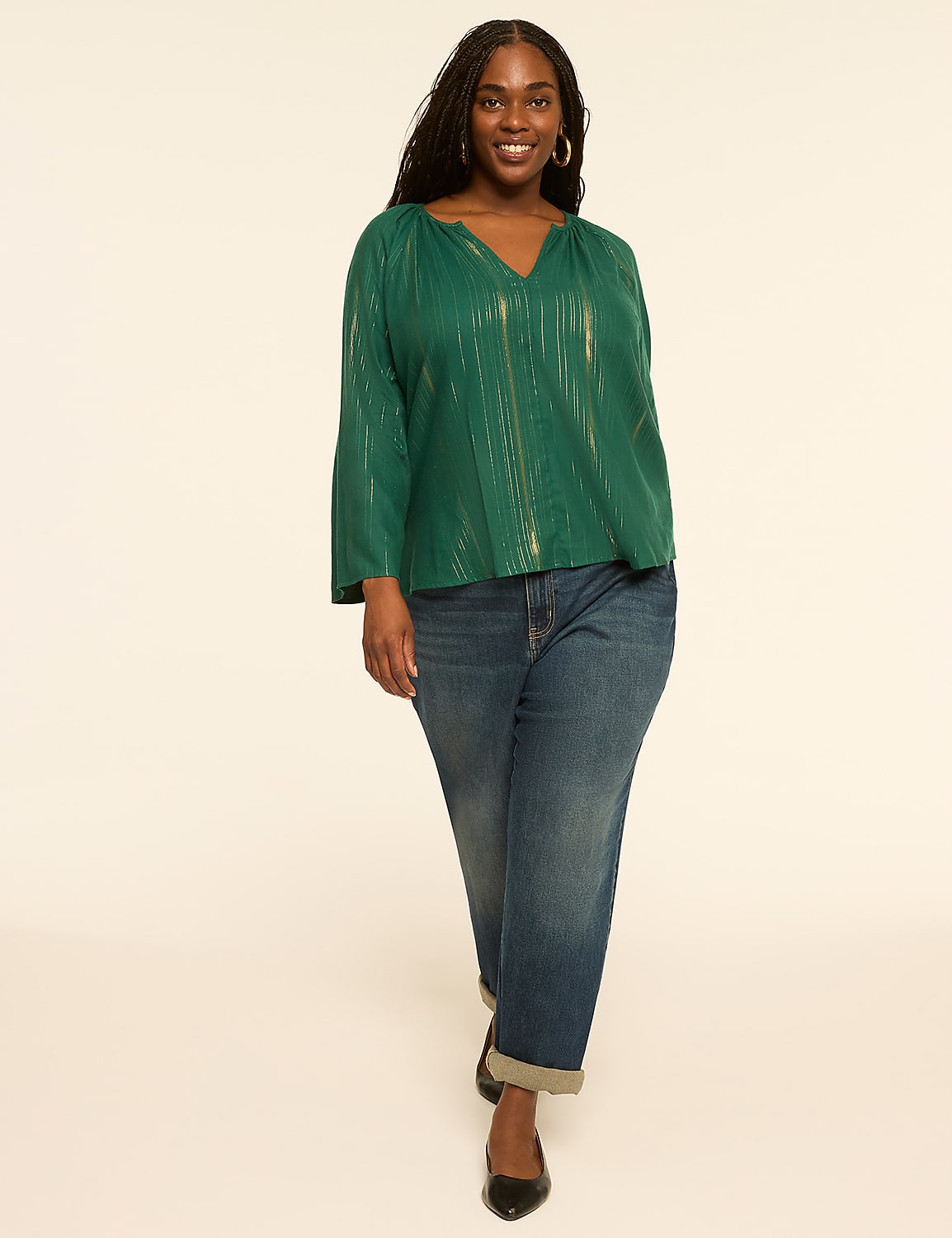 A smiling woman in a green metallic top and cuffed jeans walks forward against a plain cream background. Product Image 3