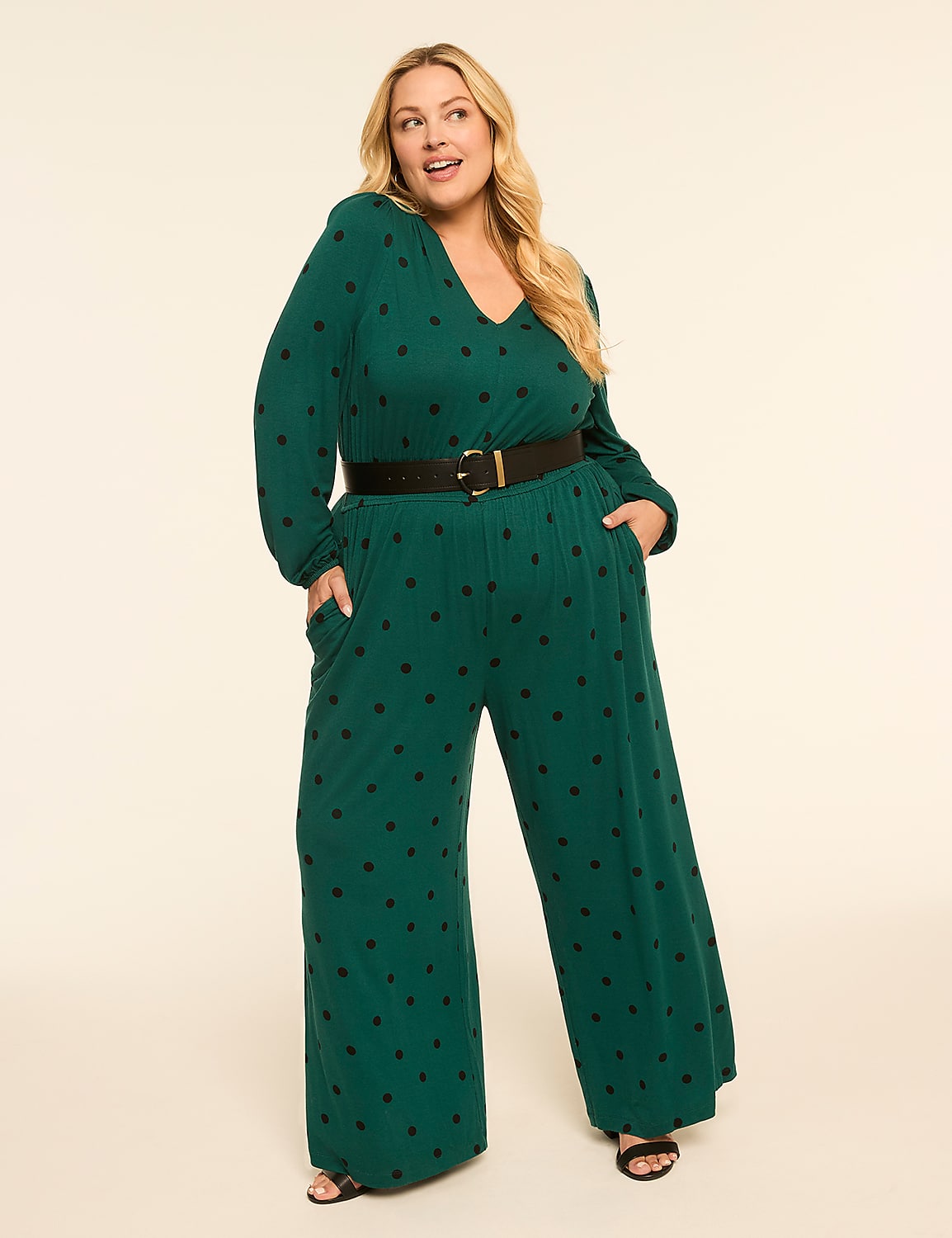 A woman in a green polka-dot jumpsuit with a black belt stands against a plain, light-colored background. Product Image 1