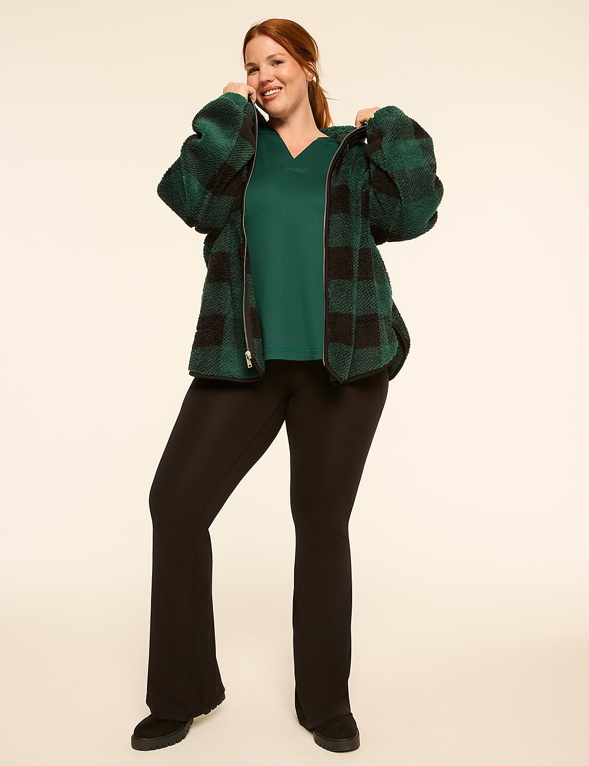 A smiling woman in a green scrub top, black flared pants, and a green and black buffalo plaid fuzzy jacket stands against a plain, light-colored background. Product Image 3