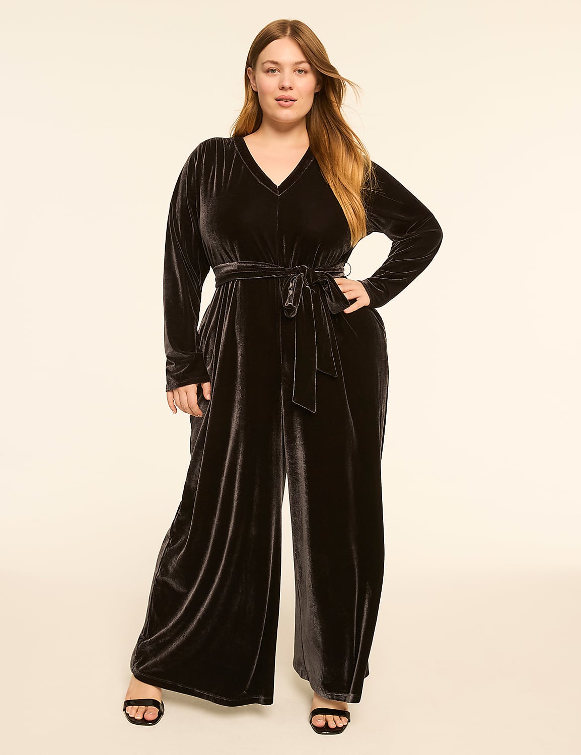 A woman in a black velvet jumpsuit stands against a plain, light-colored background. Product Image 1