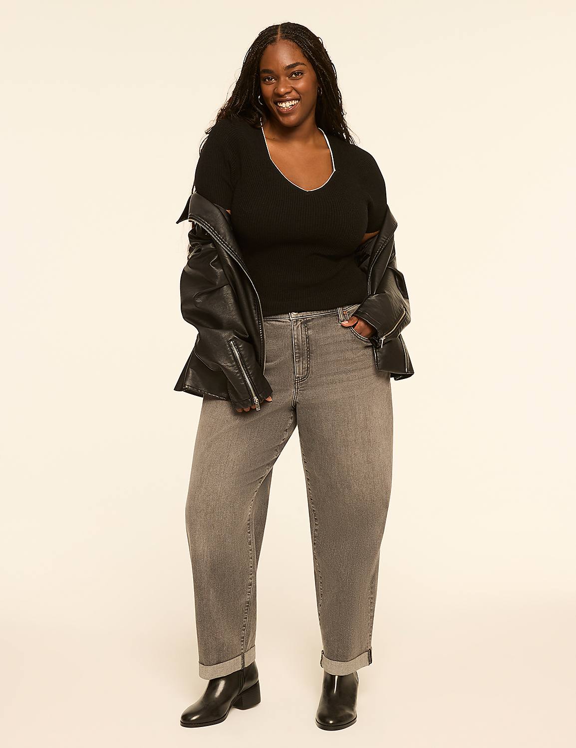 A smiling woman in a black top, leather jacket, and grey jeans stands against a plain, light-colored background. Product Image 3