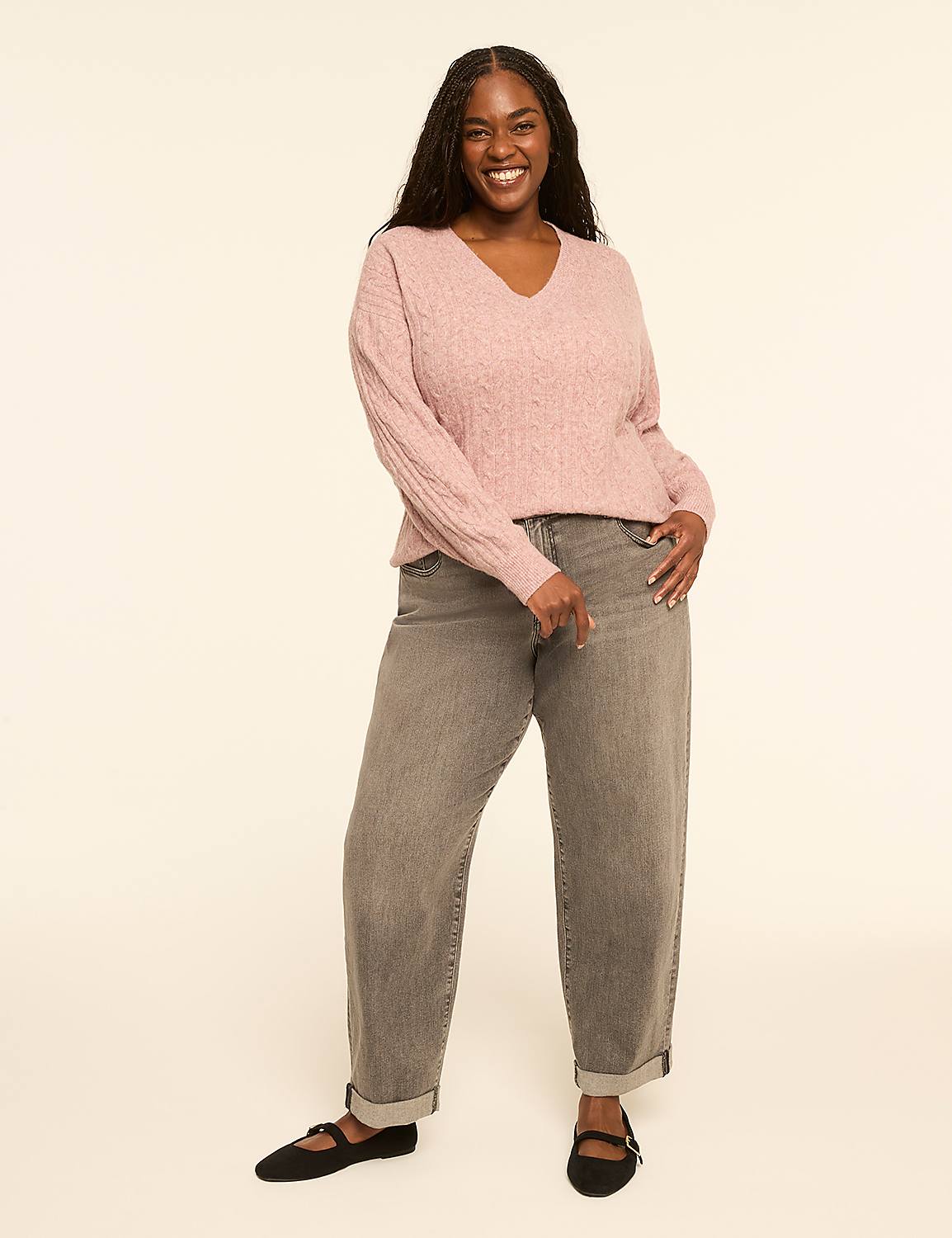 A smiling woman in a pink cable-knit sweater and gray jeans stands against a plain, light-colored background. Product Image 3
