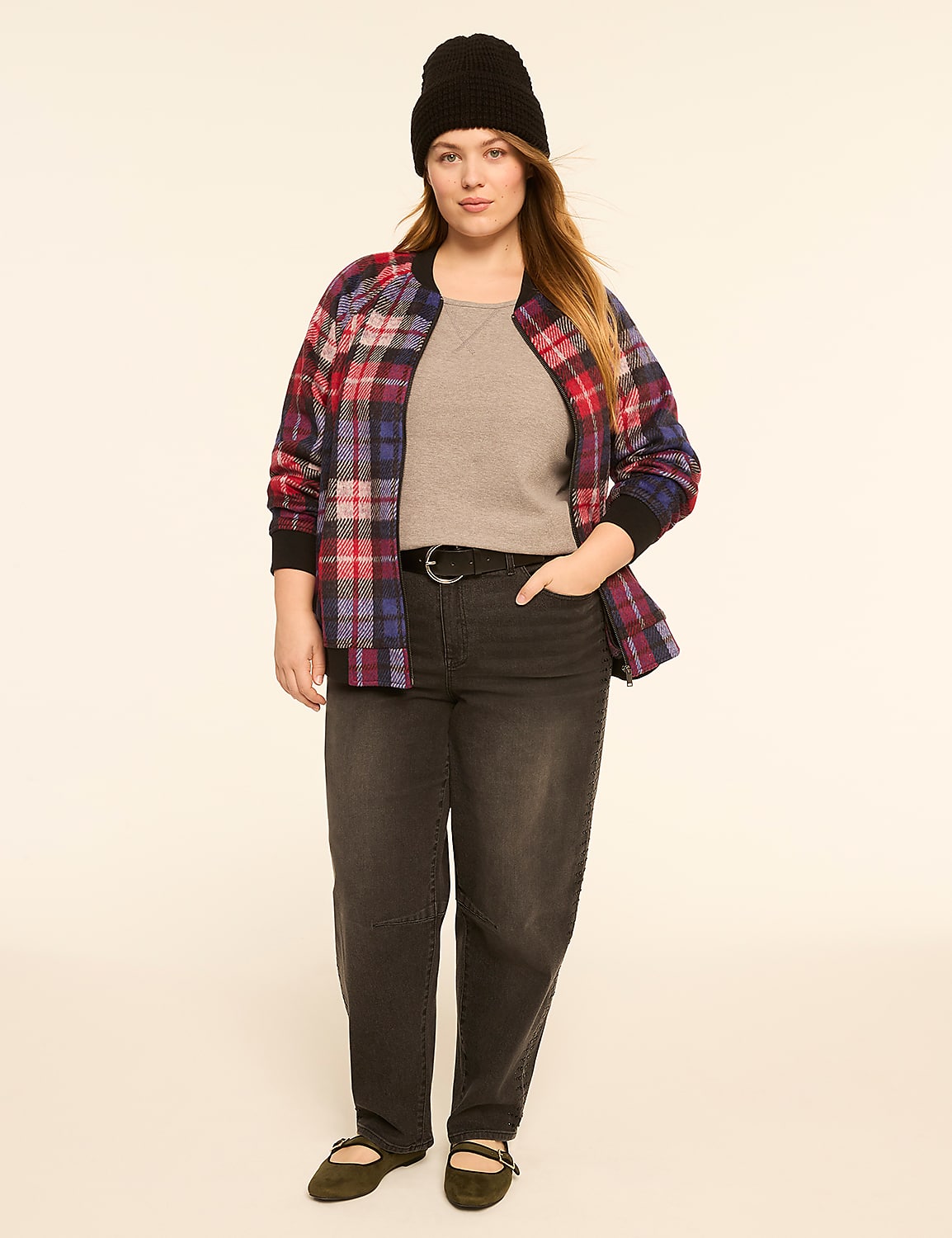 A woman in a plaid bomber jacket, gray top, black beanie, and dark jeans stands against a plain, light-colored background. Product Image 3