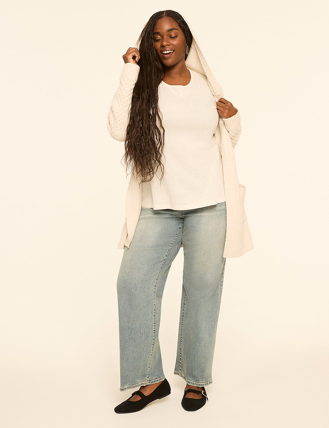 A woman with long dark hair stands in the foreground wearing a white top, a cream cardigan, and light wash jeans, against a plain cream background. Product Image 3
