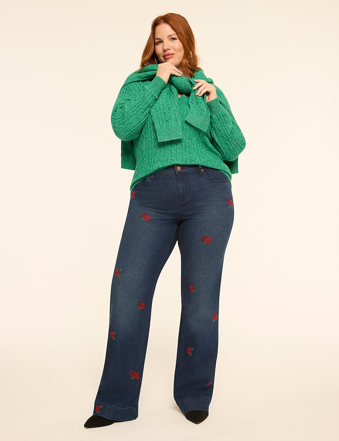 A woman in a green cable-knit sweater and embroidered jeans stands against a plain, light-colored background. Product Image 3