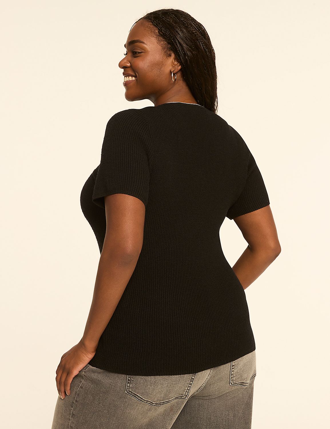 A woman in a black ribbed top and grey jeans smiles over her shoulder against a plain, light-colored background. Product Image 2