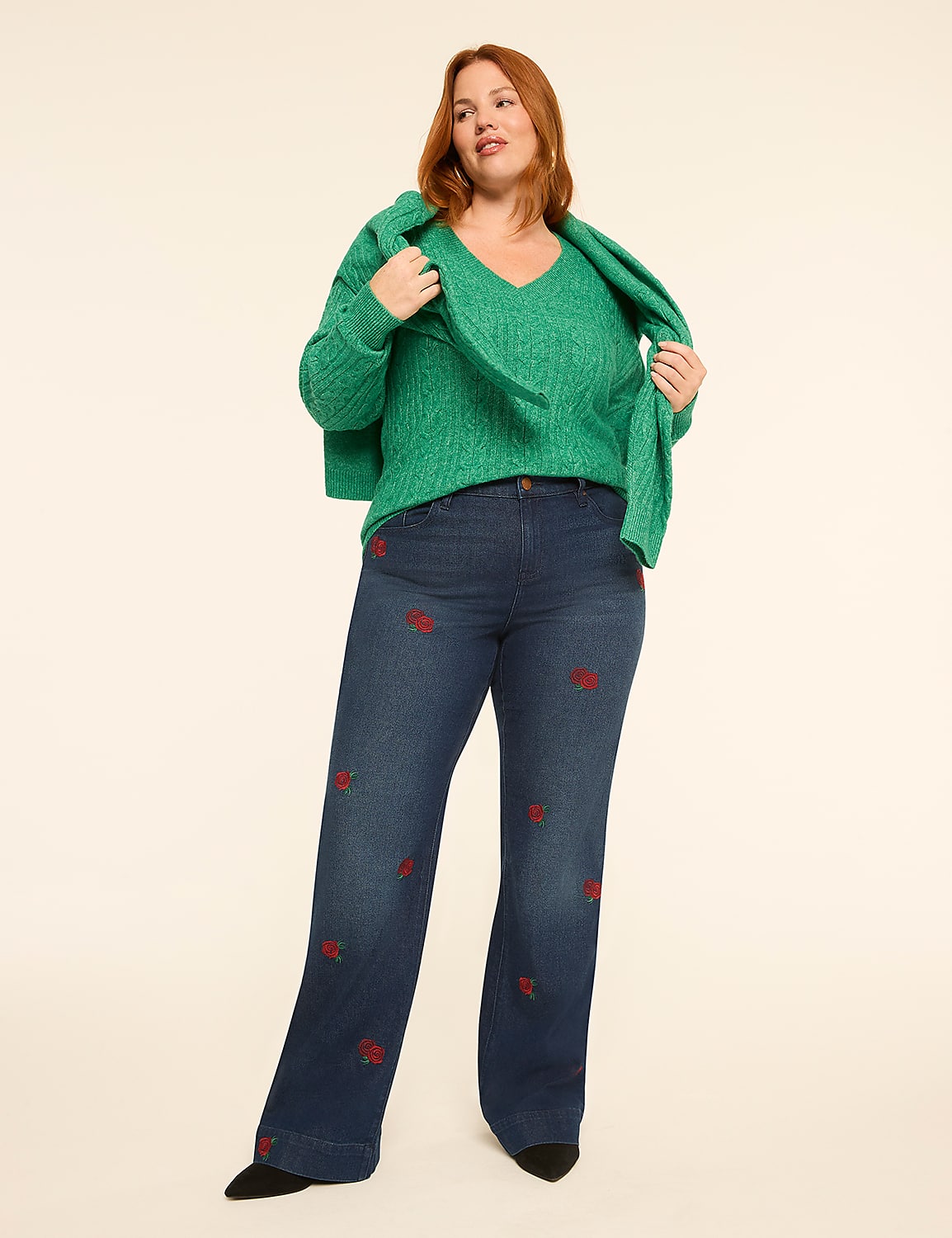 A woman in a green sweater and embroidered jeans stands against a plain, light-colored background. Product Image 3