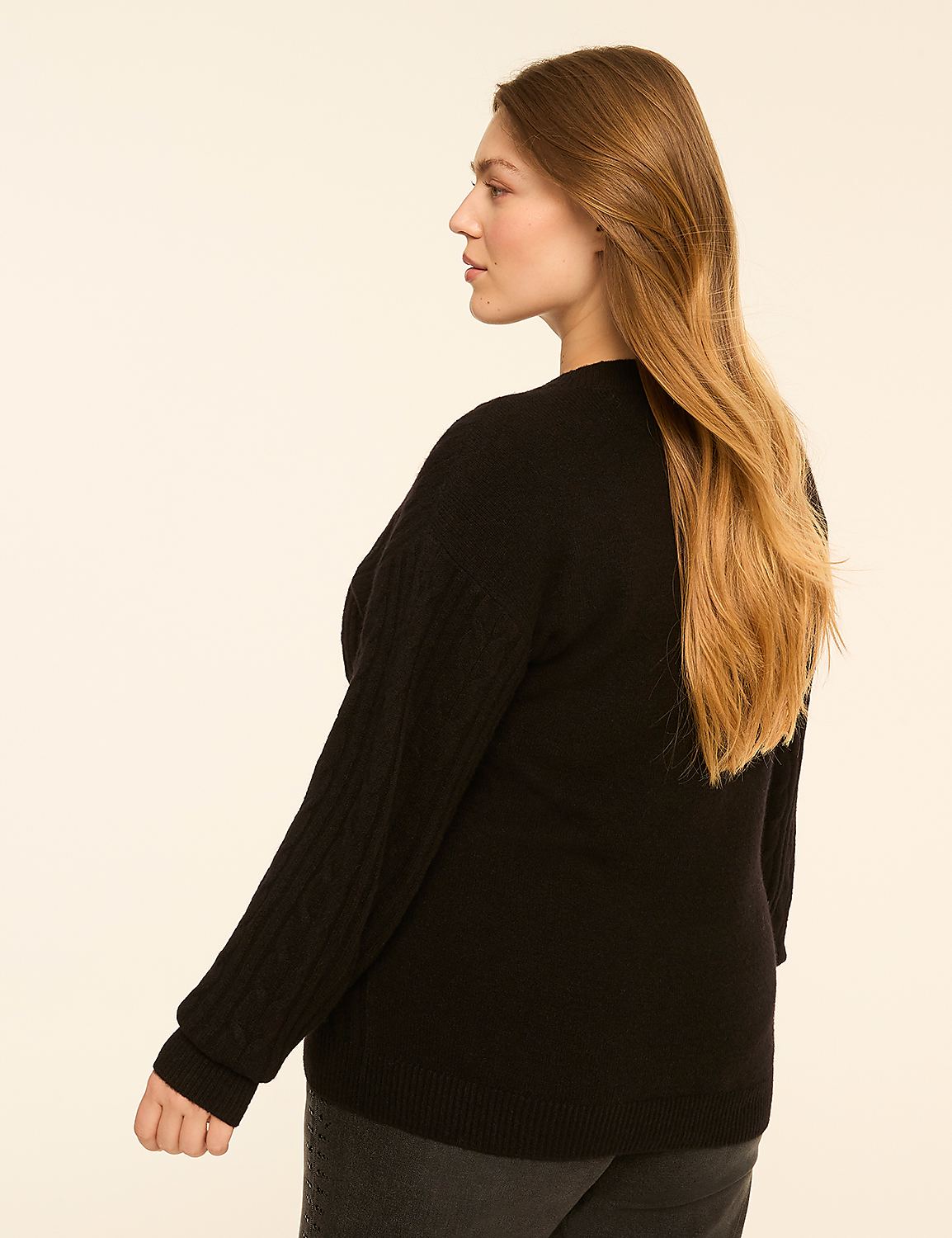 A woman in a black cable-knit sweater and dark jeans stands against a plain, light-colored background. Product Image 2