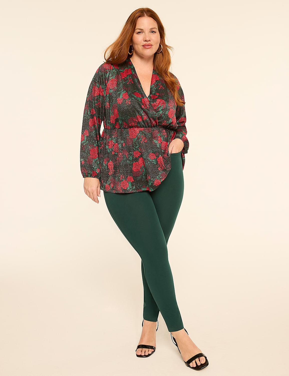 A woman with red hair poses in a floral, sparkly wrap top and dark green pants against a plain, light background. Product Image 3