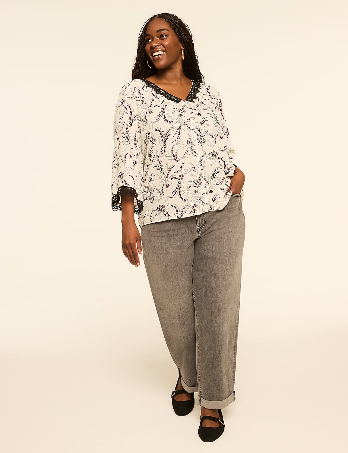 A smiling woman in a patterned top and gray jeans stands against a plain, light-colored background. Product Image 3