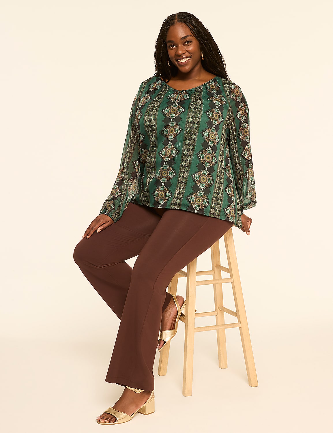 A smiling woman with dark hair, wearing a patterned green blouse and brown pants, sits on a wooden stool against a plain, light-colored background. Product Image 3