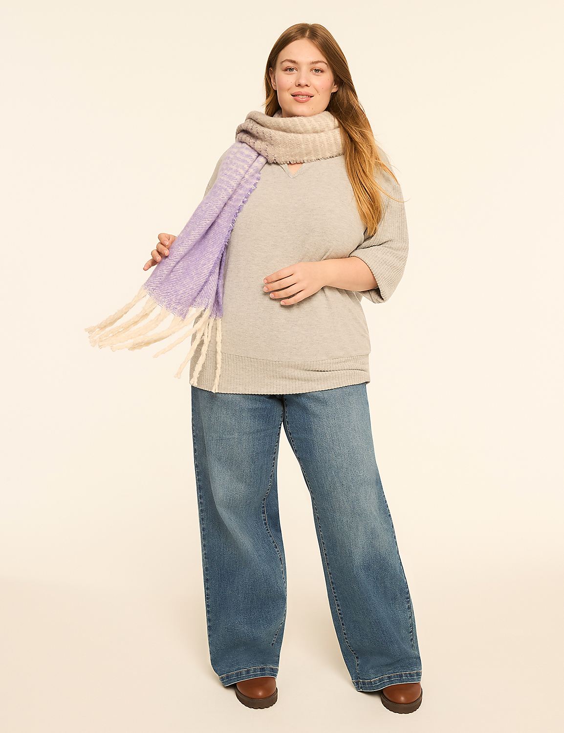 A woman in a light gray sweater and blue jeans stands in the foreground, holding a purple and cream striped scarf, against a plain, light-colored background. Product Image 3
