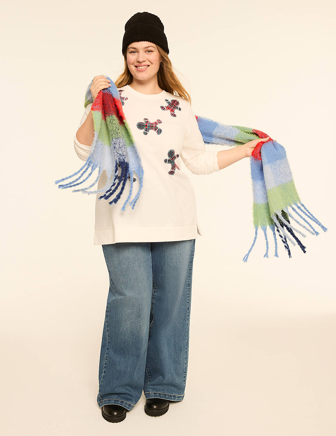 A woman in a white sweater with gingerbread man appliques, blue jeans, and a colorful scarf stands against a plain, light-colored background. Product Image 3