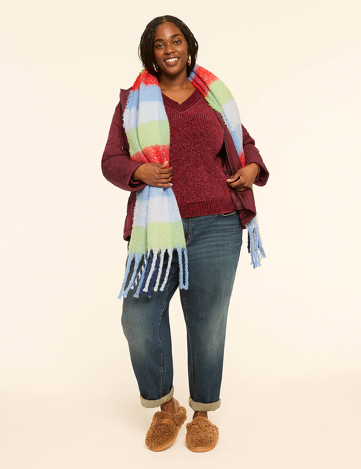 A smiling woman in a burgundy sweater, jacket, and jeans stands in front of a plain, light-colored background, accessorized with a colorful plaid scarf and fuzzy slippers. Product Image 3