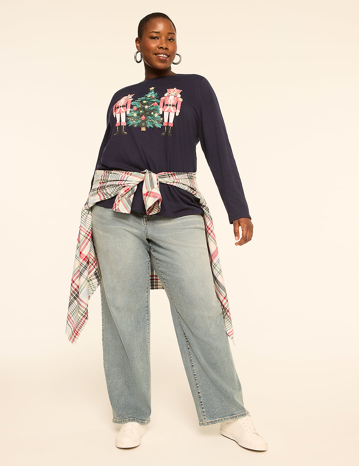 A woman in a navy long-sleeved shirt with a Christmas graphic and light-wash jeans stands against a plain, light-colored background. Product Image 3