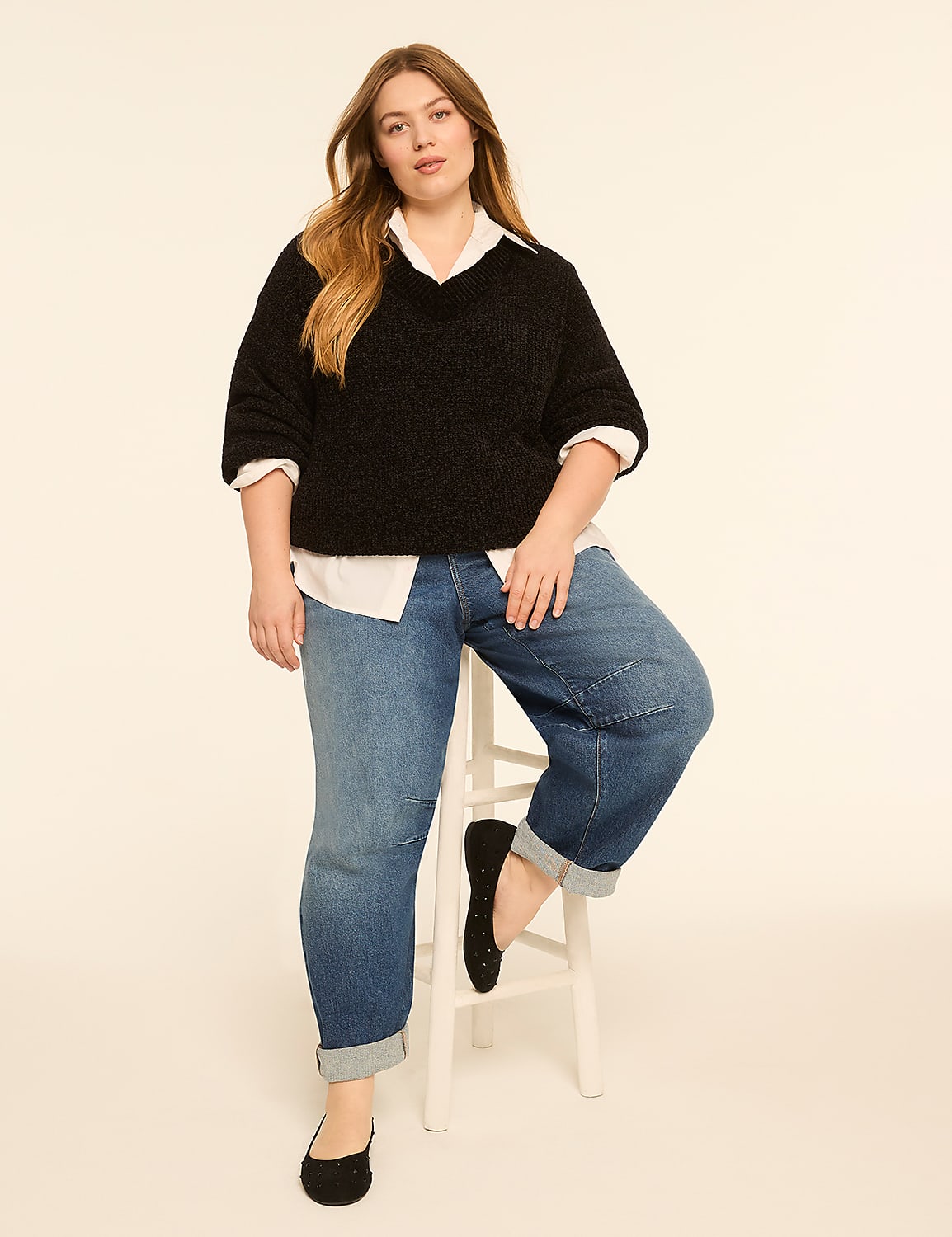 A woman in a black sweater and jeans sits on a white stool against a cream-colored background. Product Image 3