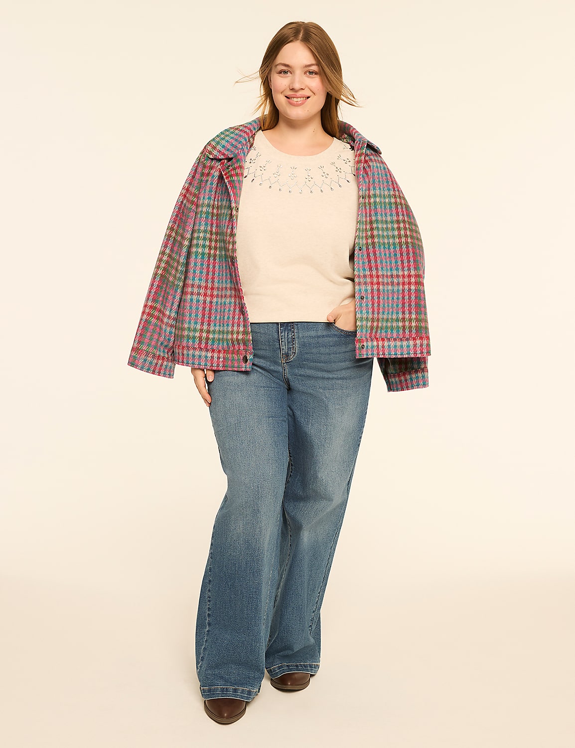 A smiling woman in a cream sweater and blue jeans stands against a plain, light-colored background, wearing a colorful plaid jacket. Product Image 3