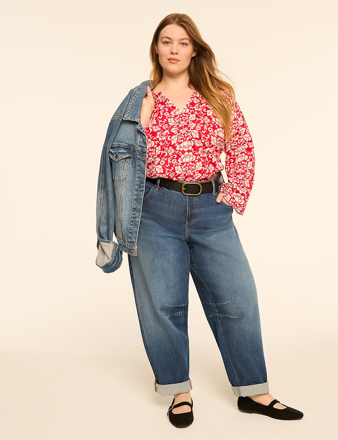 A woman in a floral blouse and jeans stands against a plain, light-colored background, with a denim jacket draped over her shoulder. Product Image 3