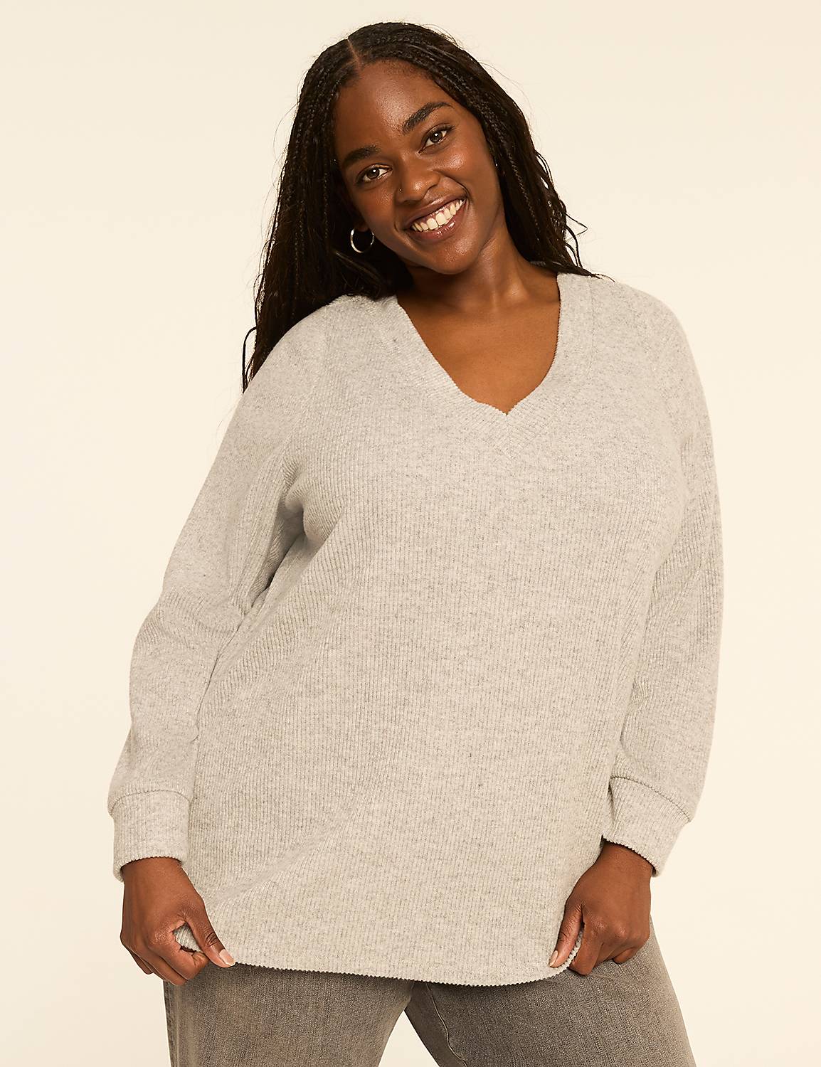 A smiling woman with dark braided hair wears a light gray v-neck sweater and gray pants against a plain beige background. Product Image 1