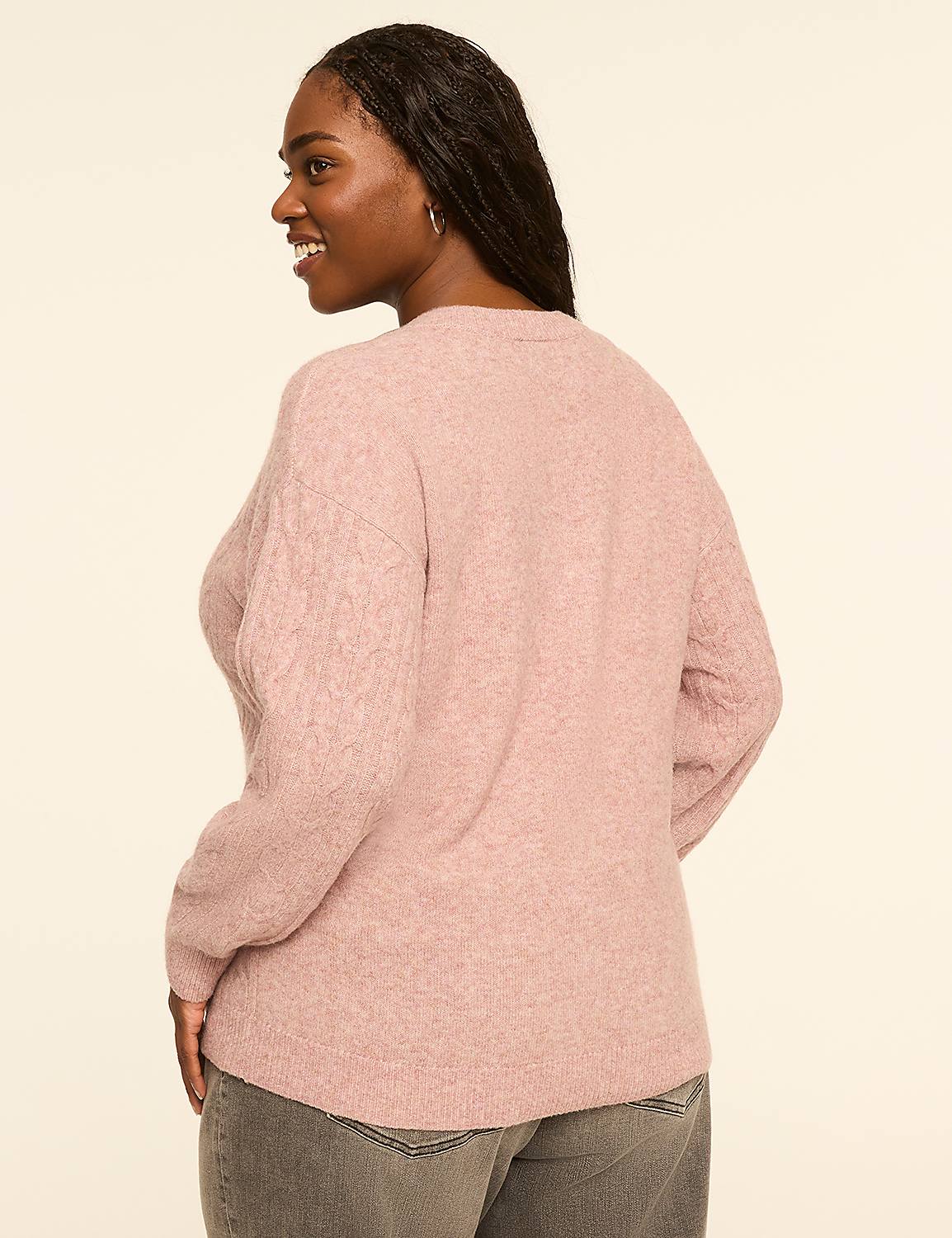A woman in a pink cable-knit sweater and gray jeans stands against a plain, light-colored background. Product Image 2