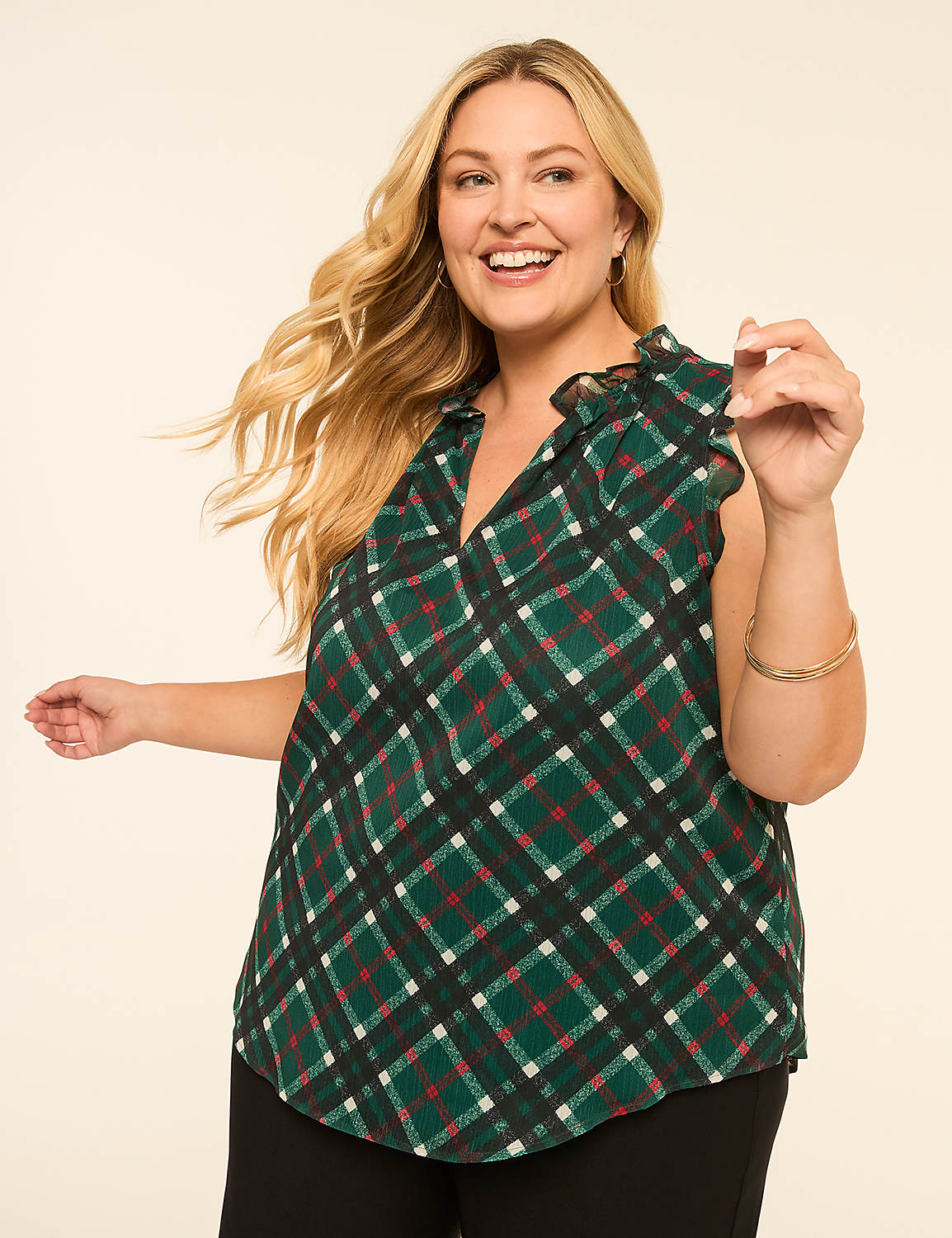 A smiling woman with blonde hair wears a green plaid top with ruffled sleeves, standing against a plain cream background. Product Image 1
