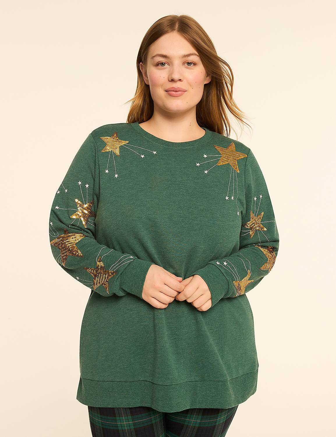 A woman in a green sweatshirt with sequined stars stands against a plain, light-colored background. Product Image 1