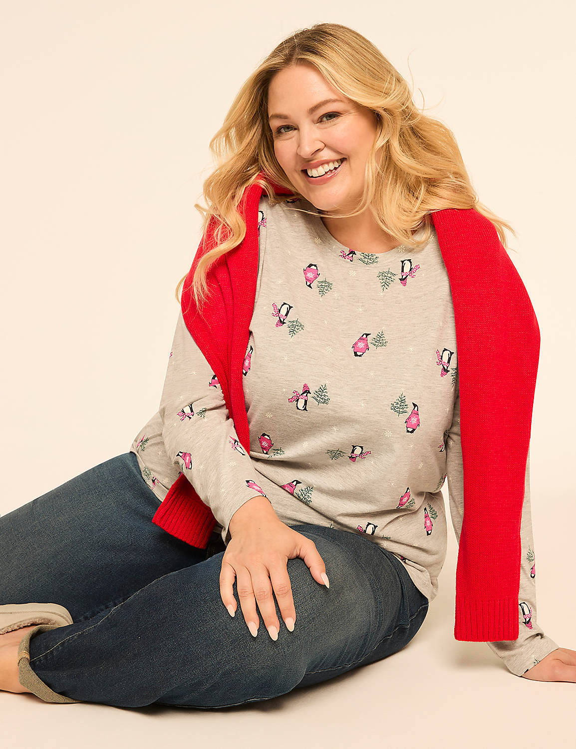 A smiling woman in a penguin-print shirt and jeans sits against a plain, light-colored background with a red sweater draped over her shoulders. Product Image 3