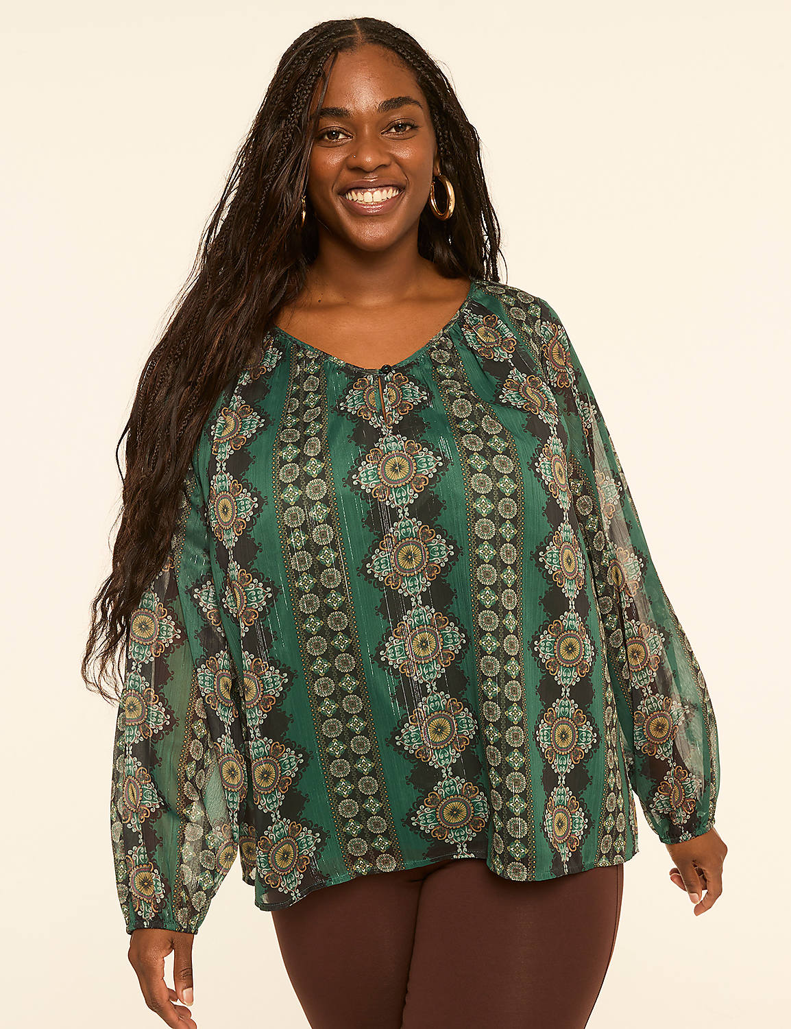 A smiling woman with long dark hair wears a flowing green patterned blouse and brown leggings against a plain cream background. Product Image 1