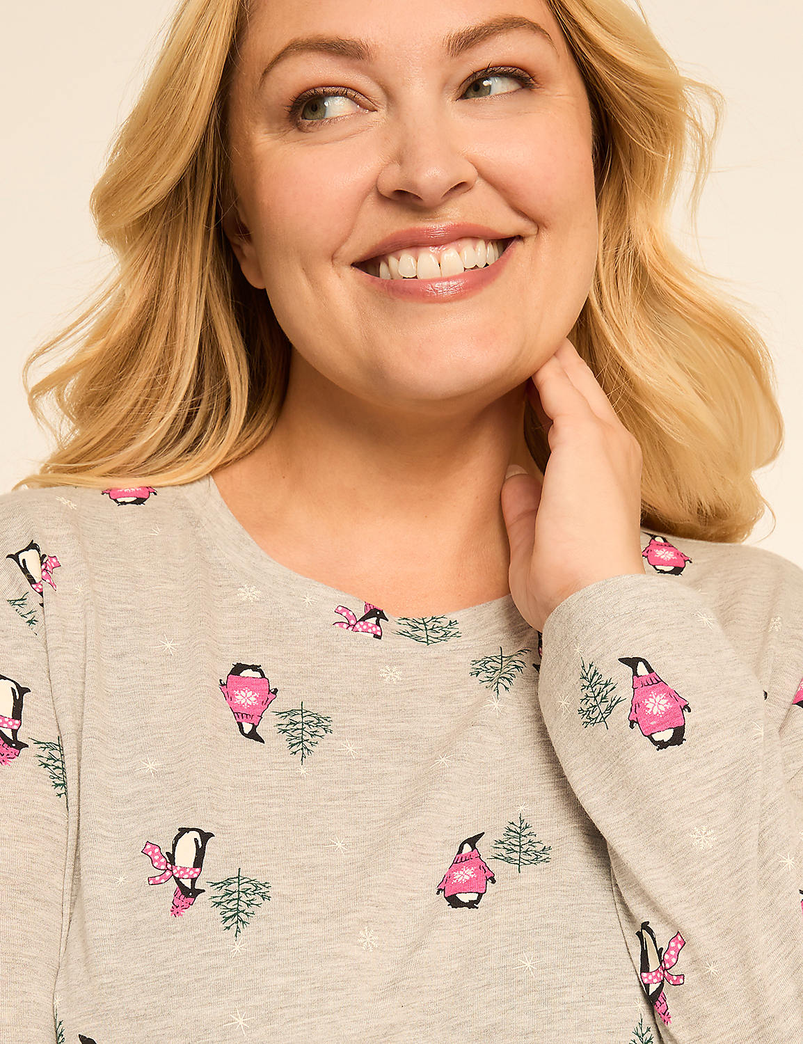 A smiling woman with blonde hair touches her neck while wearing a light gray pajama top with a pattern of penguins and trees against a plain background. Product Image 4