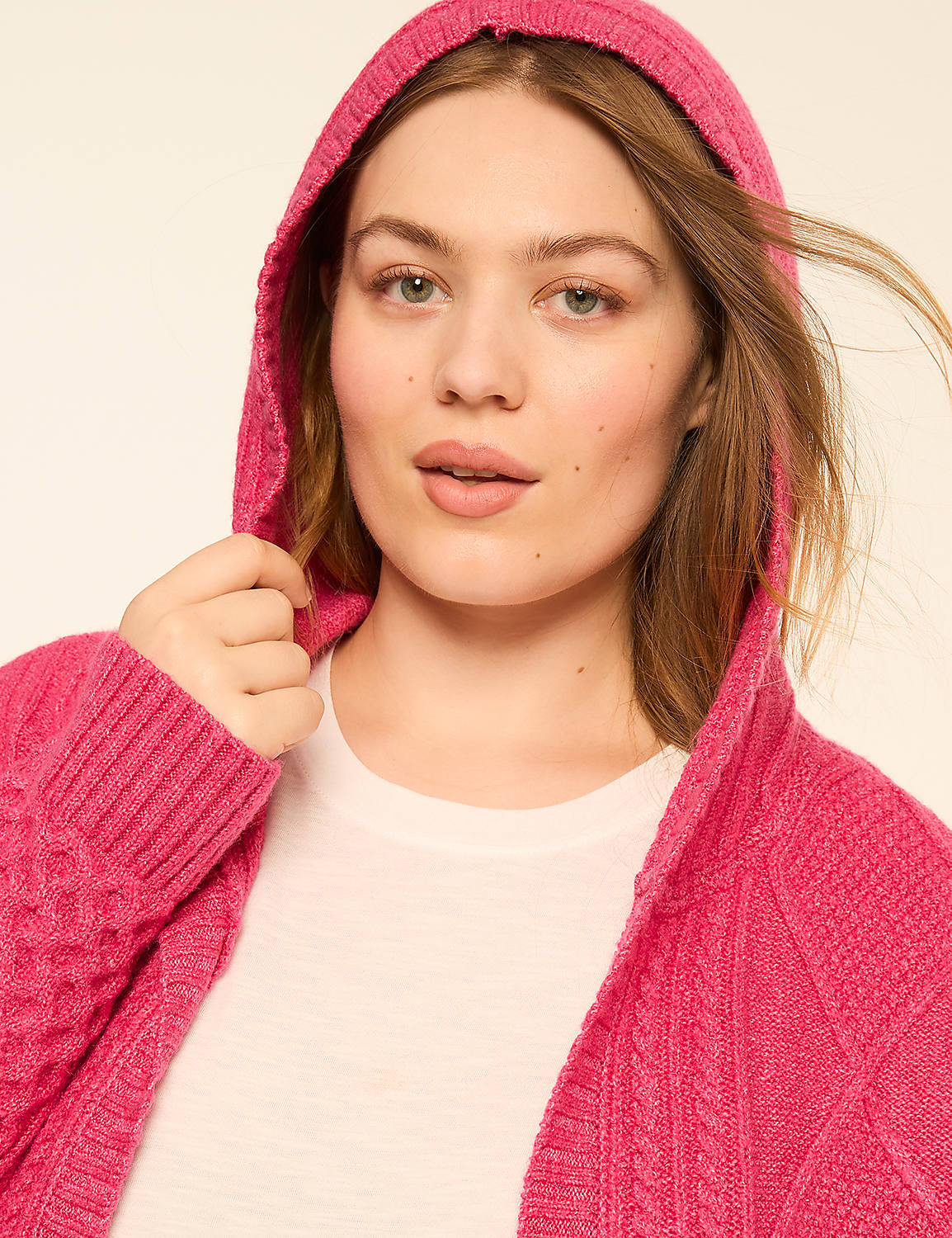 A woman in a bright pink cable-knit hooded cardigan with a white t-shirt underneath is posed against a plain, light-colored background. Product Image 4
