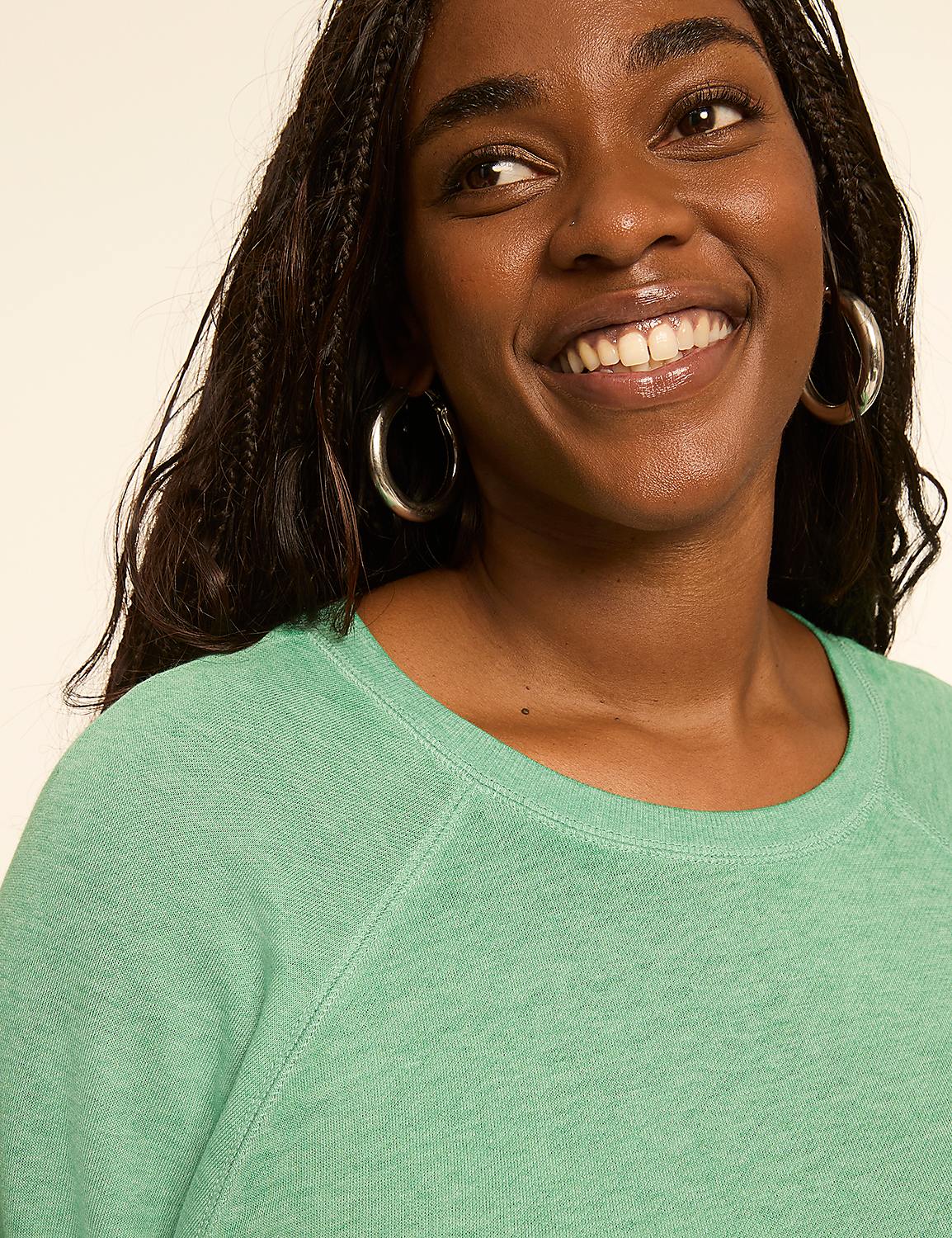 A smiling woman with braided hair and hoop earrings wears a green sweatshirt against a plain, light-colored background. Product Image 4