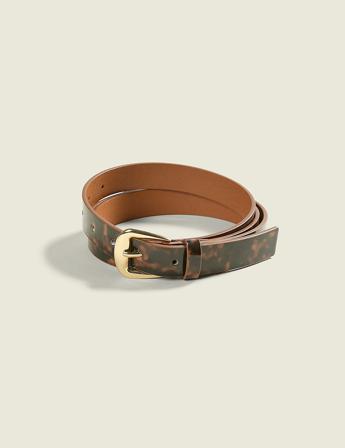 A tortoiseshell patterned belt with a brass buckle lies coiled on a plain, light brown background. Product Image 2