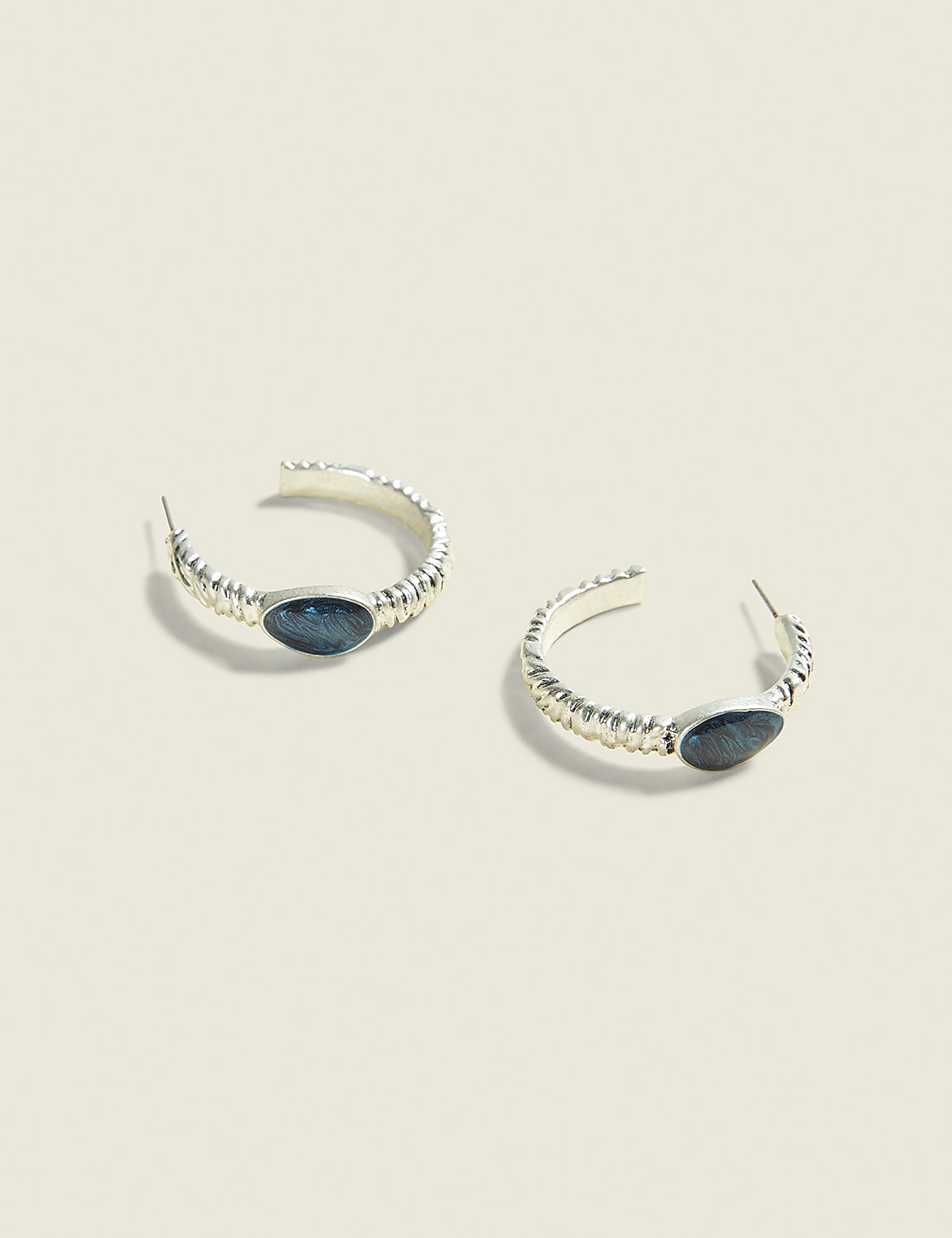 A pair of silver hoop earrings with dark oval stones are displayed against a soft, light brown background. Product Image 1