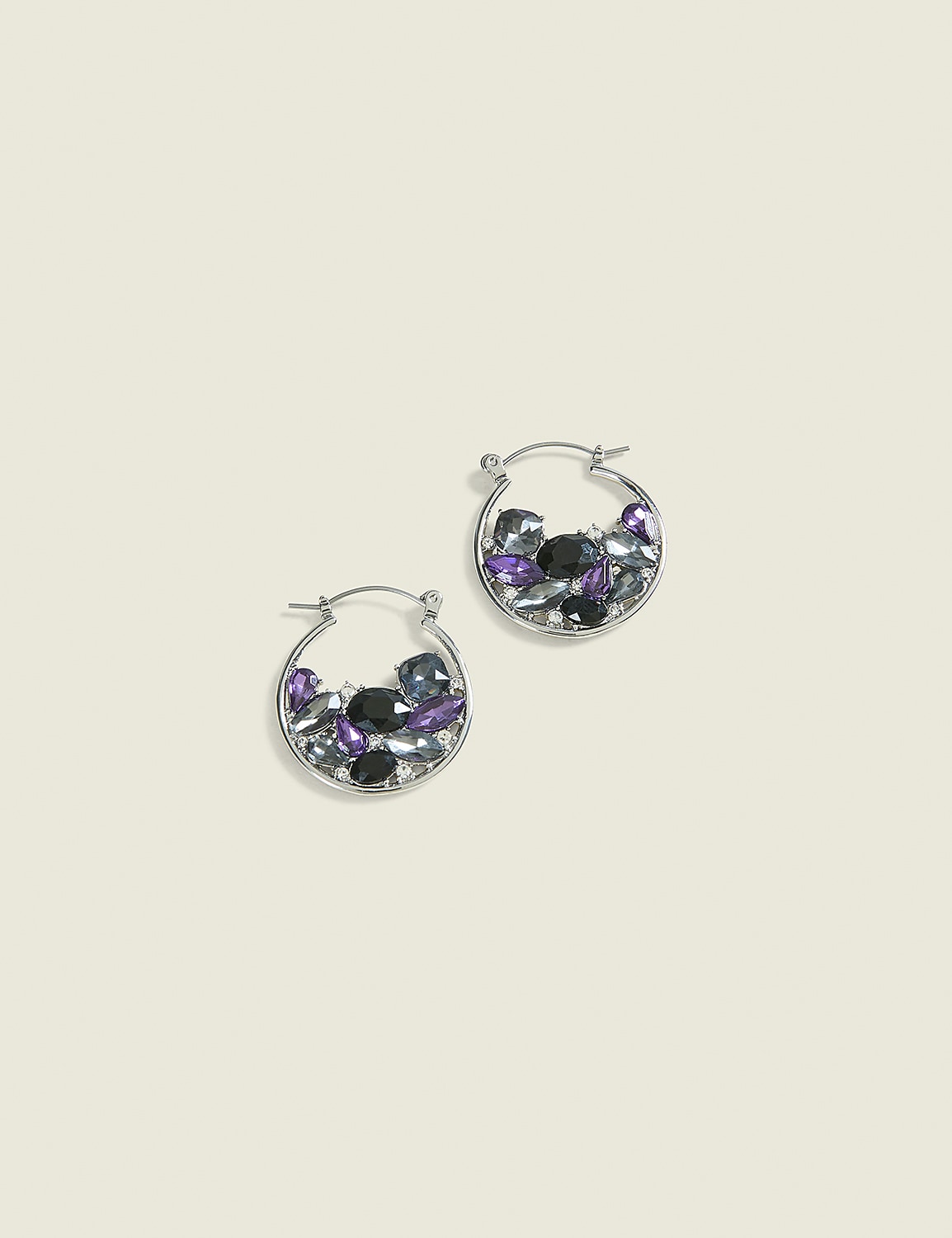 A pair of silver hoop earrings filled with purple, black, and clear stones rest on a pale yellow background. Product Image 1