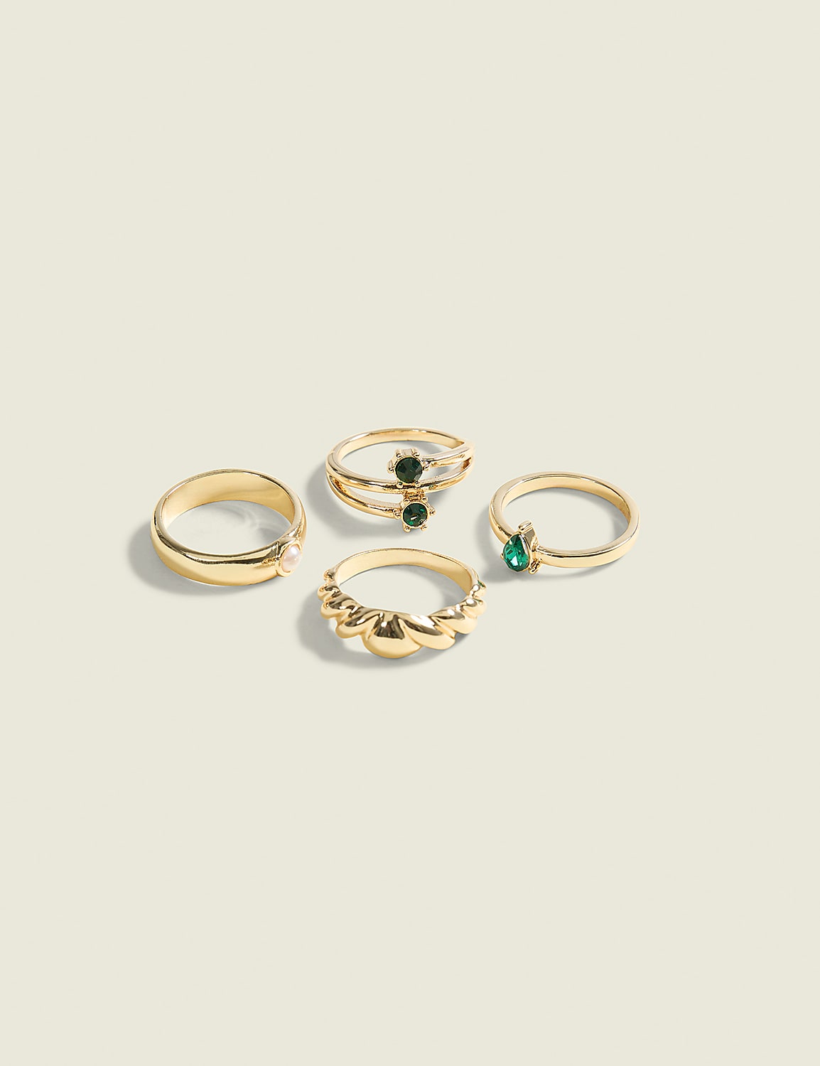 Four gold rings, two with green stones, are arranged on a plain, light-colored background. Product Image 1
