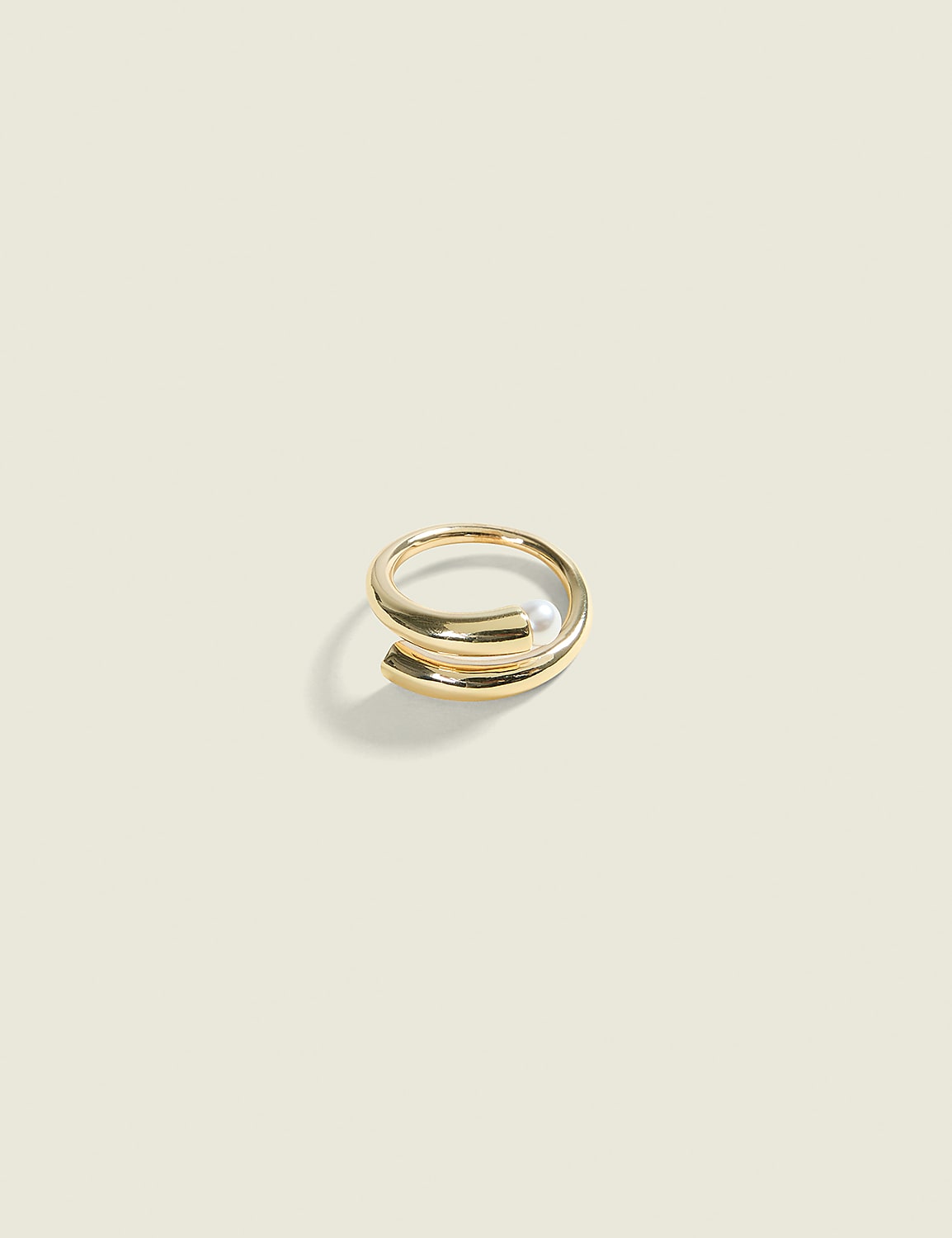 A gold spiral ring with a pearl sits on a pale yellow background. Product Image 1