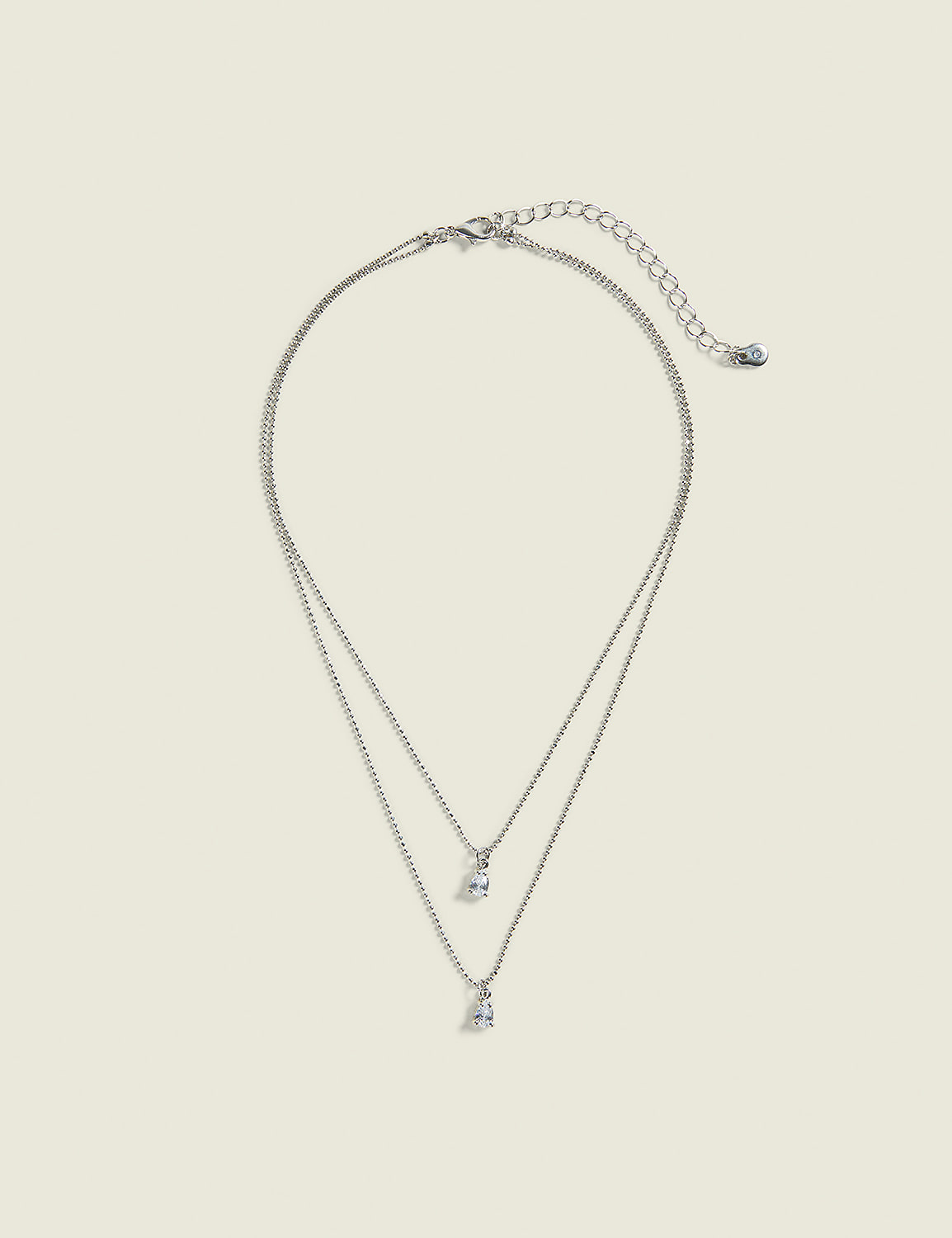 A delicate silver layered necklace with two small diamond pendants hangs against a plain, light beige background. Product Image 1