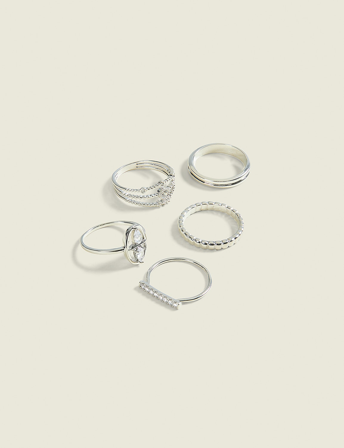 Five silver rings, some with intricate designs and others plain, are arranged on a pale, textured background. Product Image 1