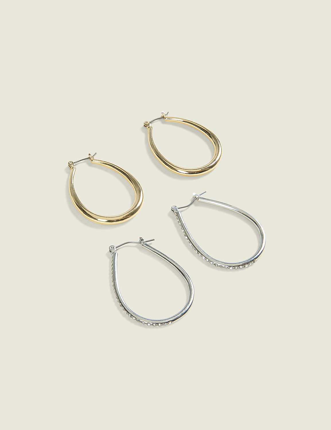 Two pairs of teardrop-shaped hoop earrings, one gold and one silver with rhinestones, rest on a pale, textured background. Product Image 1