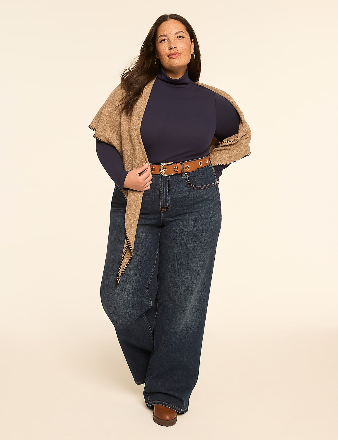 A woman in a navy turtleneck, wide-leg jeans, and a brown belt stands against a plain, light-colored background, draped in a tan shawl. Product Image 3