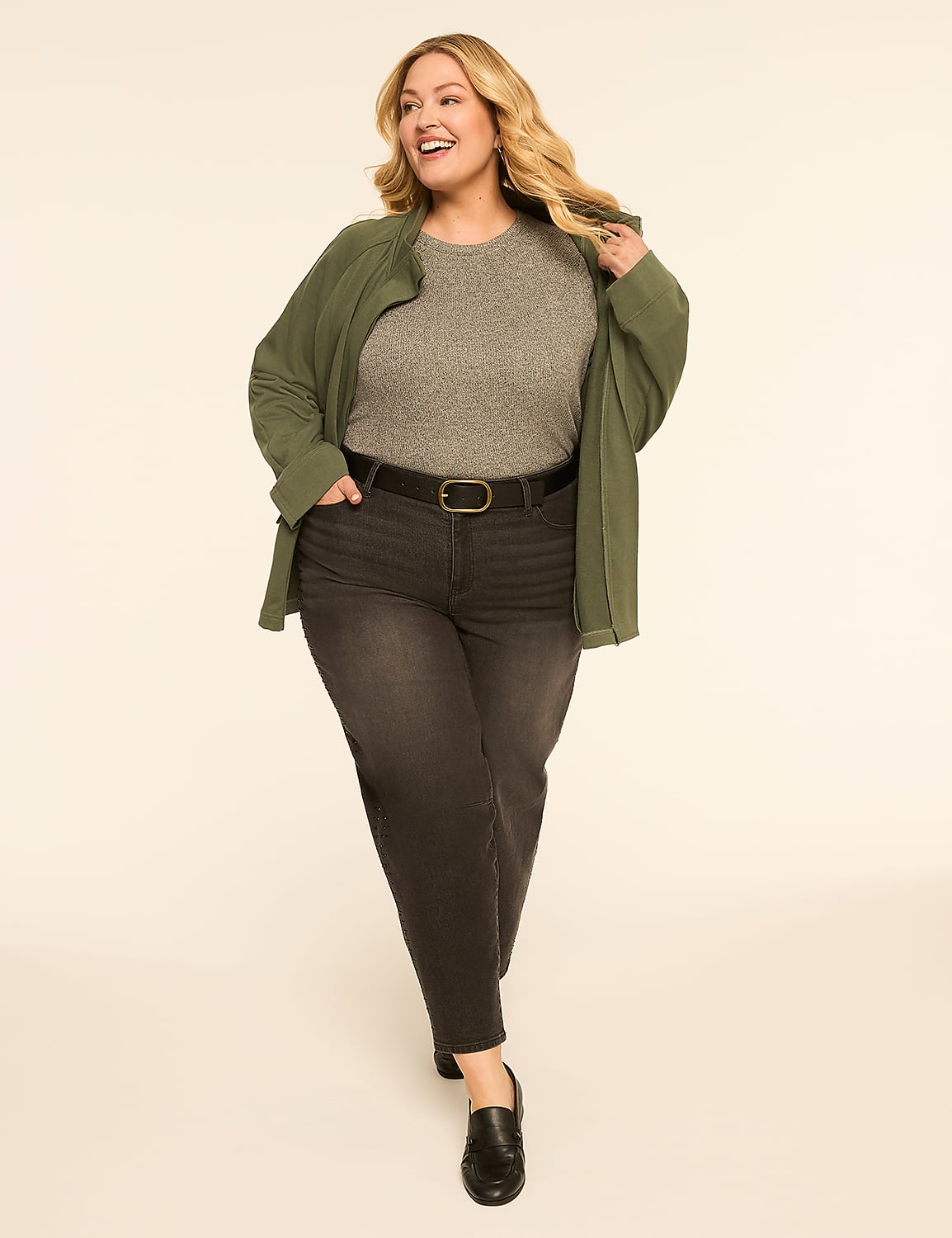 A smiling woman in a grey top, dark jeans, and a green jacket stands against a plain, light-colored background. Product Image 3