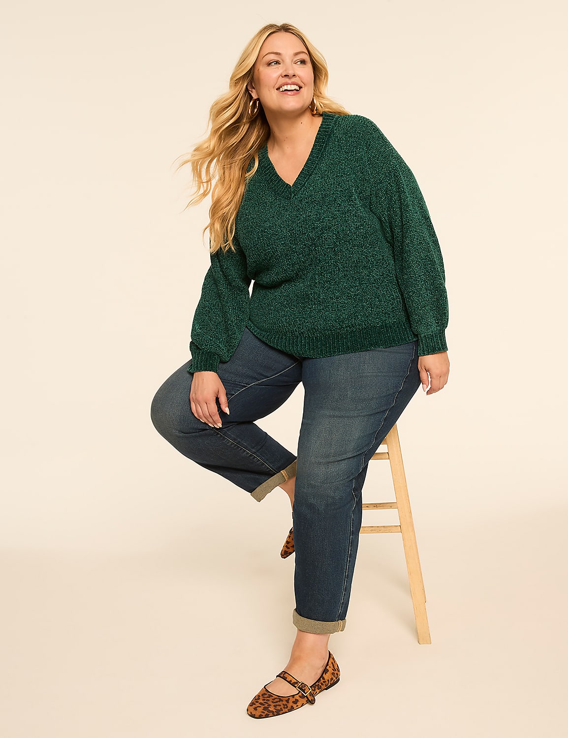 A smiling woman in a green sweater and jeans sits on a stool against a plain, light-colored background. Product Image 3