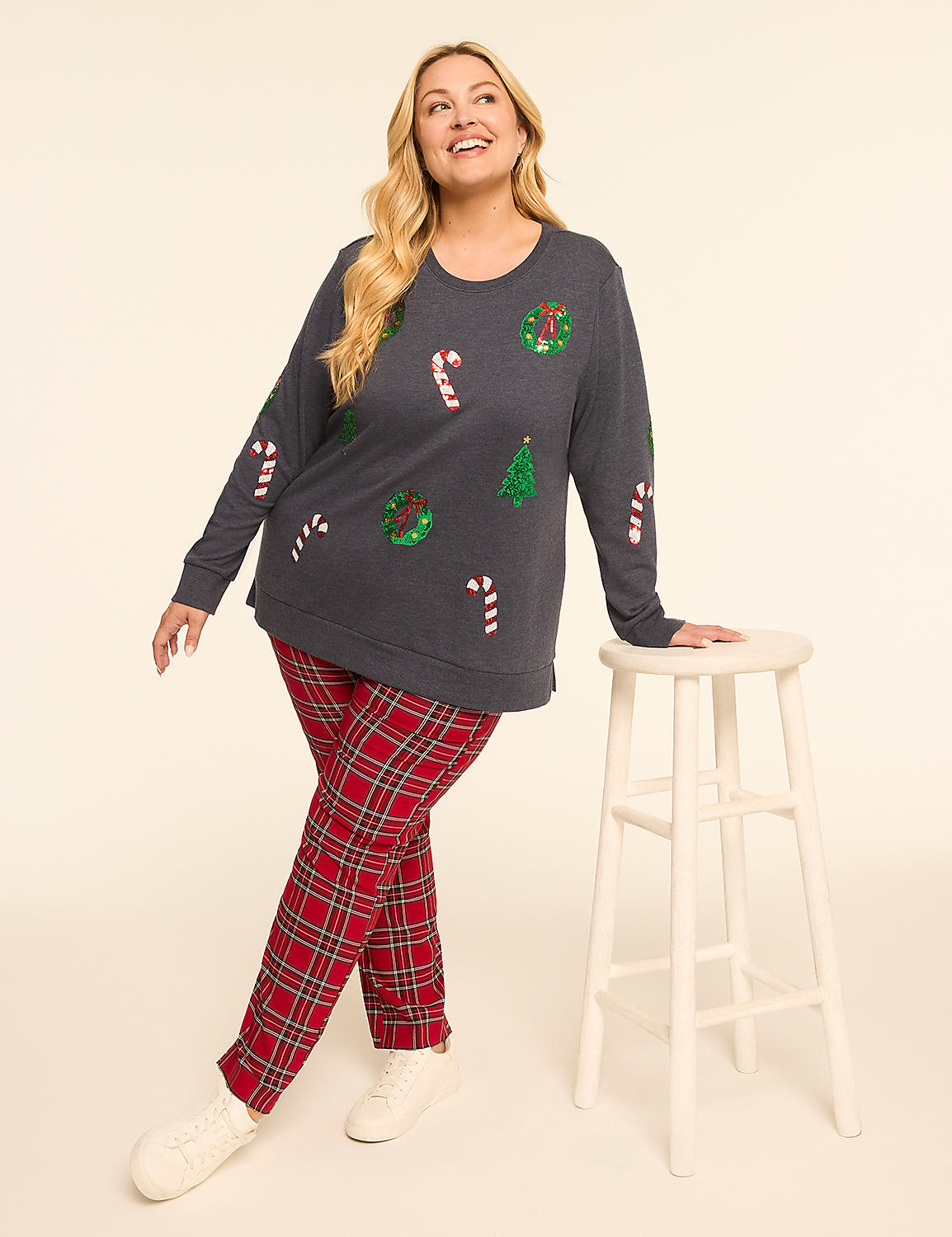 A woman in a festive Christmas-themed sweater and plaid pants poses next to a stool against a plain, light-colored background. Product Image 3