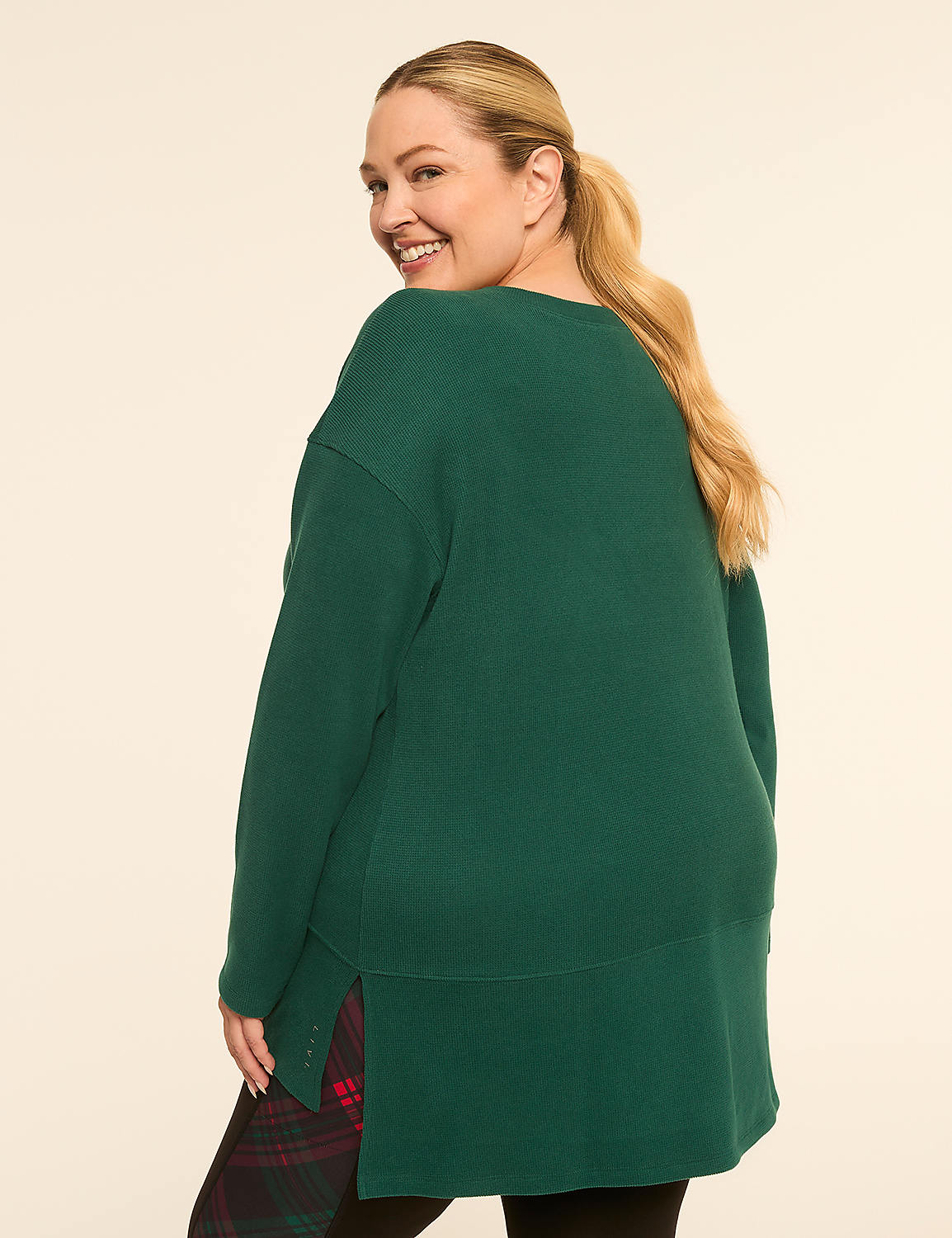 A woman in a green sweater and plaid skirt smiles over her shoulder against a plain, light background. Product Image 2