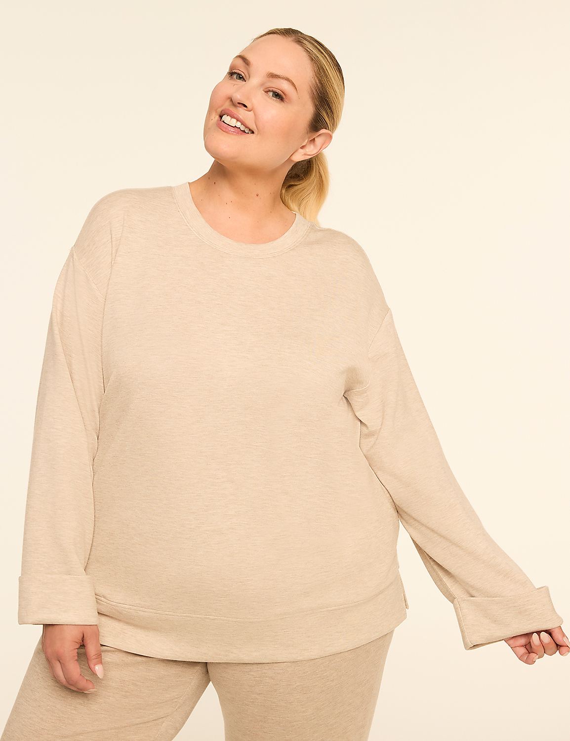 A smiling woman in a beige sweatshirt and pants stands against a plain, light-colored background. Product Image 1